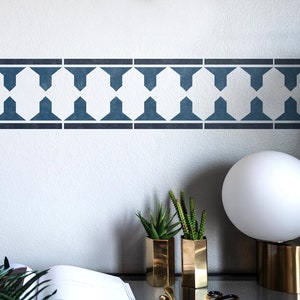 May include: A blue geometric stencil design on a white wall. The stencil is a repeating pattern of hexagons and triangles. Two small gold planters with green succulents are in the foreground.