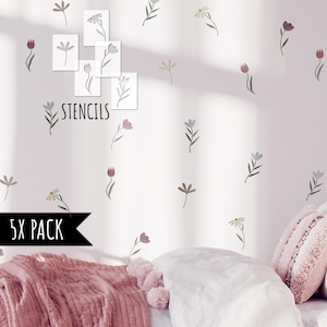 Puede incluir: Una pared decorada con plantillas florales y diseños de flores pintadas en tonos apagados de rosa, gris y beige. La palabra "STENCILS" es visible, junto con una etiqueta "5X PACK". Una cama con ropa de cama y almohadas rosas está en primer plano.