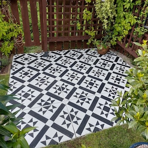 Peut inclure: Dalles de terrasse à motifs noirs et blancs. Les dalles présentent un motif géométrique répété avec des triangles et des rectangles. La terrasse est entourée de verdure et d'une clôture en bois.