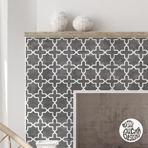 May include: A grey fireplace mantel with a white geometric pattern wallpaper. The wallpaper has a repeating pattern of stars and squares. Two white ceramic vases are on the mantel.