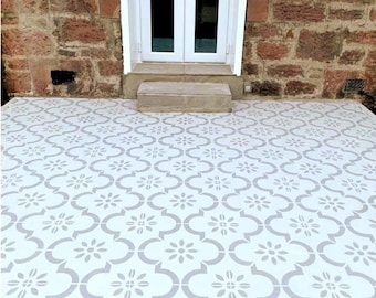 May include: White and gray patterned tile flooring with a floral design. The tiles are laid out in a repeating pattern, creating a decorative surface. The flooring is in front of a white door with gold handles and a brick wall.