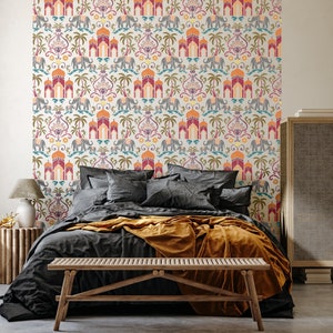 May include: A bedroom featuring a bed with a black duvet and a mustard yellow throw. The bed is positioned in front of a wall adorned with white and colourful wallpaper featuring a repeating pattern of elephants, arches, and palm trees. A wooden bench is placed in front of the bed.
