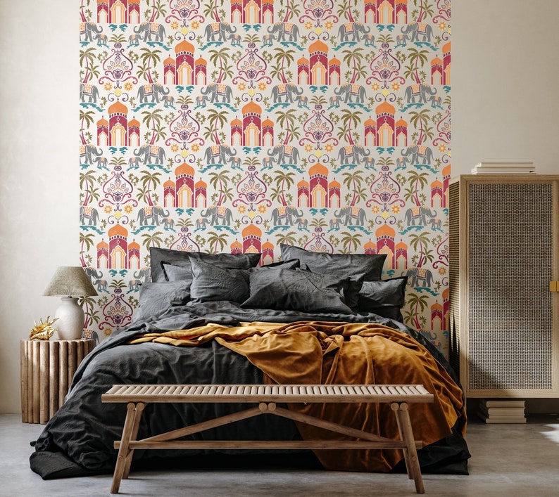 May include: A bedroom featuring a bed with a black duvet and a mustard yellow throw. The bed is positioned in front of a wall adorned with white and colourful wallpaper featuring a repeating pattern of elephants, arches, and palm trees. A wooden bench is placed in front of the bed.