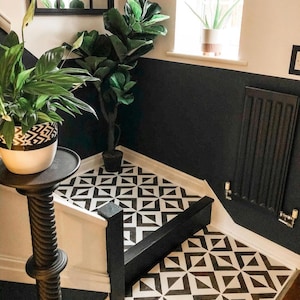 May include: A staircase with black and white geometric tiles, a black wall, and a black radiator. A potted plant sits on a black stand. Another plant is in a white pot with a black geometric design.