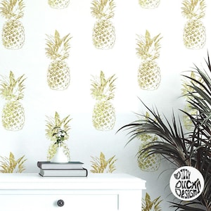 May include: Gold pineapple wallpaper with a white background. The wallpaper features a repeating pattern of pineapples. A small potted plant and a white table with books are in the foreground.