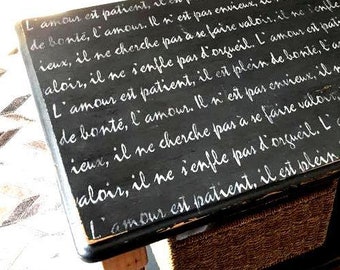 May include: A black wooden table with white cursive text. The table has a woven basket underneath and a light-colored wooden leg. The text appears to be a quote about love.