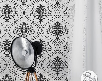 May include: Black and white damask pattern stencil with a white background. The stencil is shown on a wall with a white curtain and a black lamp.