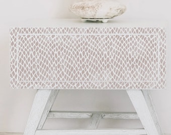 May include: White nightstand with a snakeskin pattern on the front. The nightstand has a lower shelf and angled legs.