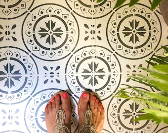 May include: A pair of gold sandals with red toe nails on a black and white patterned tile floor.