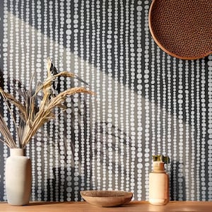 Pode incluir: Uma cena interior em tons neutros com um vaso com plantas secas, uma pequena tigela de madeira e uma garrafa decorativa. O fundo é uma parede com um padrão repetitivo de pontos brancos sobre um fundo cinza escuro. Uma cesta tecida também é visível.