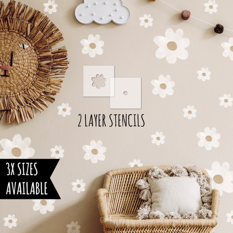 May include: A beige wall adorned with white daisy stencils and a woven lion head. The text "2 LAYER STENCILS" and "3X SIZES AVAILABLE" are displayed. A wicker chair and cloud light are also visible.