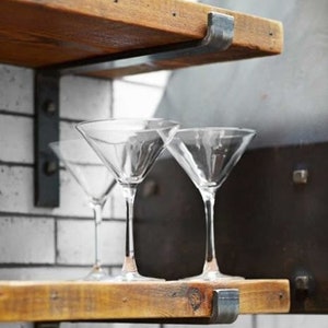 May include: Two wooden shelves with metal brackets, supporting three martini glasses. The shelves are made of reclaimed wood and have a rustic look.