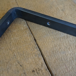 Peut inclure: Équerre de tablette en métal noir avec trois trous pour le montage. L'équerre est en forme de L et a un bord arrondi.