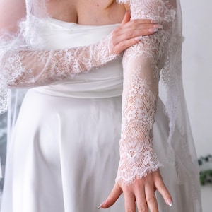 May include: A white satin dress featuring a strapless bodice and long, sheer lace sleeves with intricate floral patterns and scalloped edges. The lace sleeves extend from the shoulders to the wrists, showcasing delicate embroidery and fine mesh detailing.