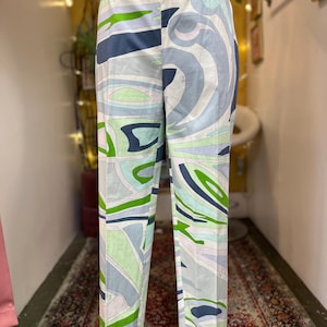 May include: Full-length trousers featuring an abstract, swirling pattern in shades of light blue, dark blue, white, and bright green. The pants have a straight-leg silhouette, a simple elasticized waistband, and a smooth, lightweight fabric construction.