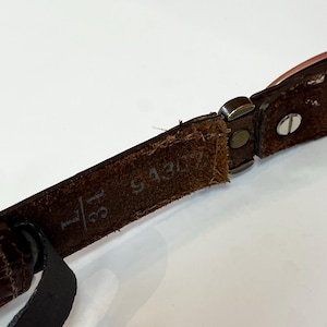 May include: Close-up of a brown leather belt with a metal buckle. The belt is marked with the size 31 and the number S4307. The leather has a textured appearance.