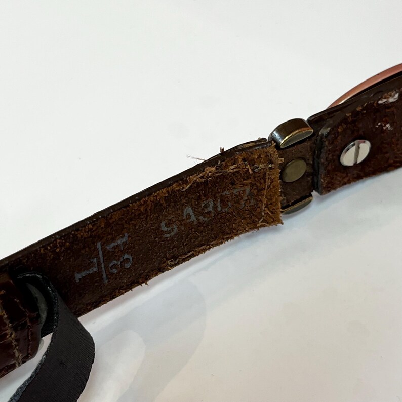 May include: Close-up of a brown leather belt with a metal buckle. The belt is marked with the size 31 and the number S4307. The leather has a textured appearance.