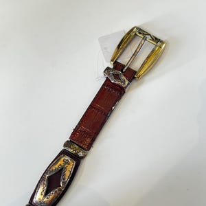 May include: A white ceramic mug with a black handle and the text "But First, Coffee" in a bold, black font. The mug is set against a blurred background, suggesting a cozy setting.