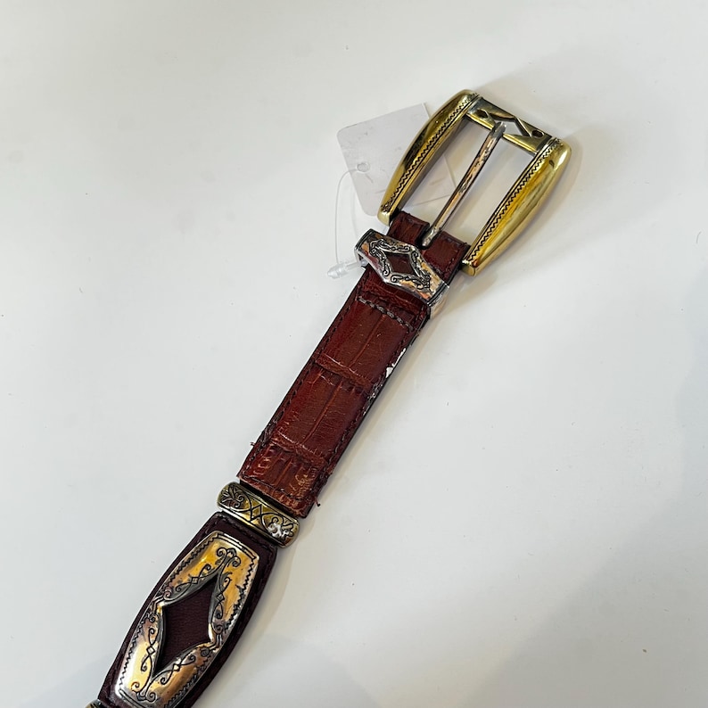 May include: A white ceramic mug with a black handle and the text "But First, Coffee" in a bold, black font. The mug is set against a blurred background, suggesting a cozy setting.