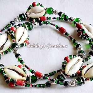 May include: A layered necklace featuring white cowrie shells, red and green beads, and silver-toned accents. The necklace has the text "Osàdàyò Creations".