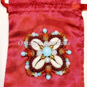 May include: A red satin drawstring bag with a beaded floral design. The design features white seashells, light blue and white beads, and gold accents. The text "Osadayo Creations" is visible.