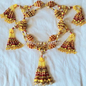 May include: A beaded garland with yellow and red beads, featuring multiple tassels. The garland is made of small, round beads and has a decorative design. The garland is hanging on a white background.