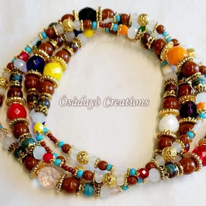 May include: A multi-strand beaded necklace with a variety of colorful beads, including brown, red, yellow, blue, and white. Gold-colored accents and the text "Osadayo Creations" are also visible. The necklace is likely handmade.