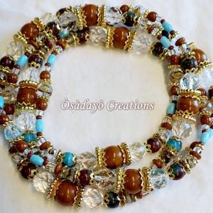 May include: A multi-strand necklace featuring brown, clear, and turquoise beads with gold-colored accents. The necklace has large, round brown beads and smaller, clear crystal beads. The text "Osadayo Creations" is visible.