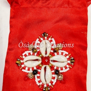 May include: Red satin drawstring bag with a beaded, shell, and gemstone embellishment. The design features four white shells, red and white beads, and gold accents. The text "Osadayo Creations" is printed on the bag.