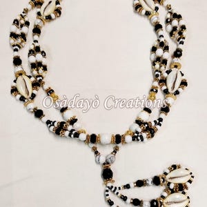 May include: A multi-strand necklace with black, white, and gold beads, cowrie shells, and a tassel. The necklace is made by Osadayò Creations.