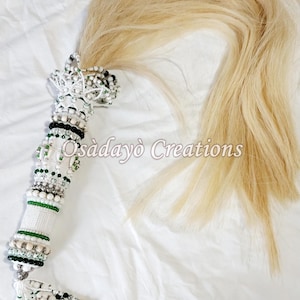 May include: A white and green beaded horsehair tassel with a white tassel at the bottom. The tassel is decorated with white and green beads, and the horsehair is a light blonde color. The text "Osadayõ Creations" is visible in the image.