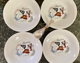 May include: Four white ceramic bowls with a blue, red, and gold design featuring a crab, shrimp, and lobster. The bowls have the text "Louisiana" and "Feed Your Soul" printed on them.