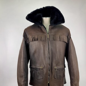 May include: Brown leather jacket with a black faux fur collar and fringe detailing. The jacket features a zip-up front, two front pockets with fringe, and a classic Western style. A vintage-inspired outerwear piece.