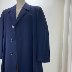 Puede incluir: Un abrigo largo azul marino con cierre de un solo botón y tres botones. El abrigo tiene un cuello clásico y mangas largas.