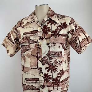 May include: A beige short-sleeved shirt with a brown and white print of palm trees and beach scenes. The shirt has a button-up collar and a pocket on the left side. The text "Aloha Towers" and "Waikiki Beach" are printed on the shirt.