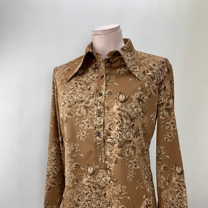 May include: A long-sleeved brown shirt with a floral print. The shirt has a collared neckline and button closure.