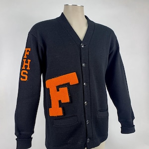 May include: Black cardigan sweater with orange felt letter "F" on the front and "FHS" on the left sleeve. The sweater has a V-neck, button closure, and two front pockets. The sweater is displayed on a mannequin.
