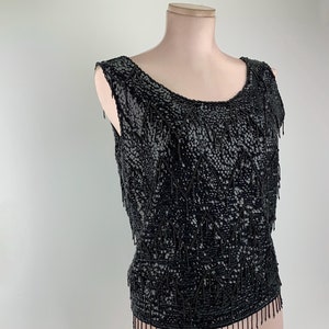 May include: A black sleeveless top with a beaded fringe design. The top is made of sequins and has a scoop neckline.