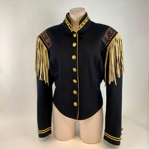 May include: Black jacket with gold trim, buttons, and shoulder fringe. The jacket features a high collar and decorative shoulder accents with a plaid pattern. The sleeves have gold stripes and buttons at the cuffs. A vintage-inspired garment.