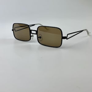 May include: Black rectangular sunglasses with brown tinted lenses. The frames are black with a thin, angular design at the temples. The arms are silver at the ends. The sunglasses are set against a white background.