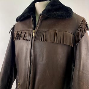 May include: Brown leather jacket with black faux fur collar and fringe detailing. The jacket features a zip-up front, two front pockets with fringe, and gold-tone hardware. A classic western-inspired outerwear piece.