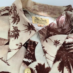 May include: A beige and brown Hawaiian shirt with a palm tree print. The shirt has a label that reads "The Fair Department Store Honolulu" and "M".