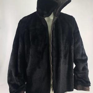 May include: A black faux fur jacket with a high collar and a full-length zipper. The jacket has brown trim on the cuffs and collar. The jacket is displayed on a mannequin.