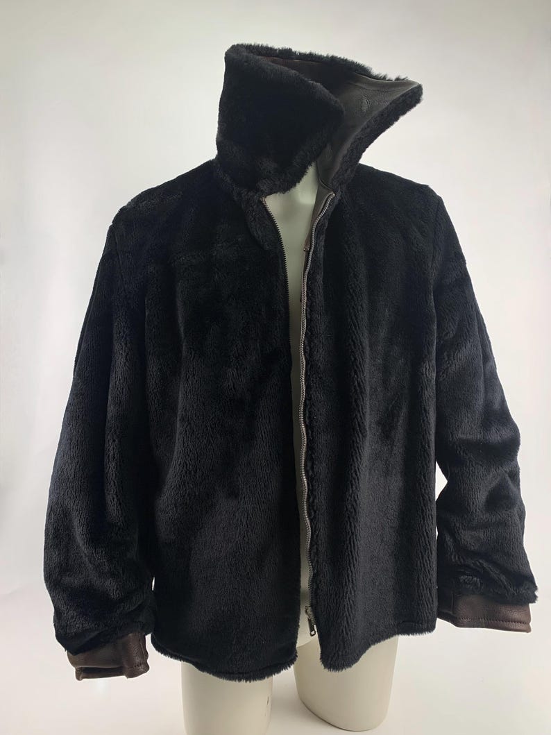 May include: A black faux fur jacket with a high collar and a full-length zipper. The jacket has brown trim on the cuffs and collar. The jacket is displayed on a mannequin.