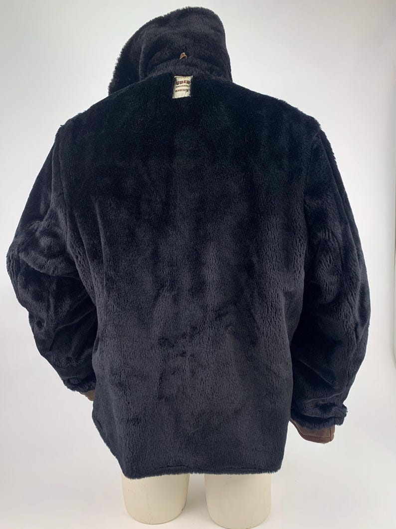 May include: Black faux fur coat with a large collar. The coat has a plush texture and a brown trim on the cuffs. A small tag is visible near the collar. The coat is displayed on a mannequin.