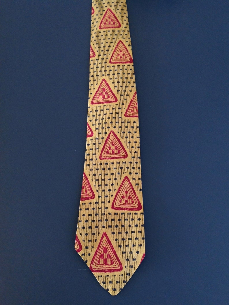 May include: A yellow tie with a repeating pattern of red triangles. The triangles have a black outline and a geometric design inside.