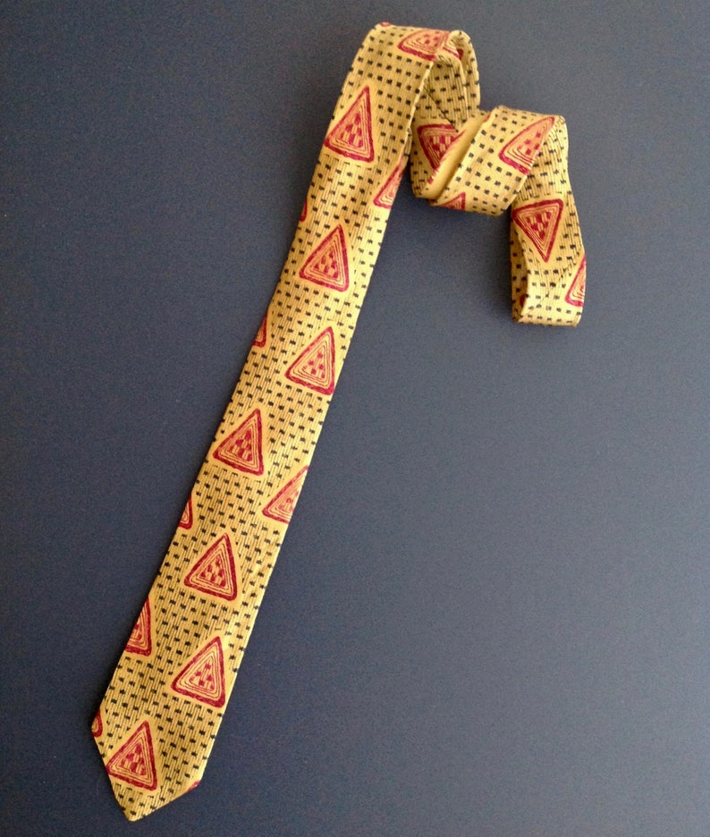May include: A yellow tie with a repeating pattern of red triangles. The tie is folded in half and the tip is pointing down.