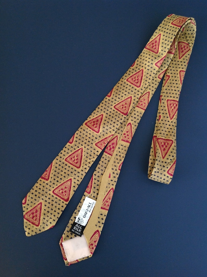 May include: A gold and red patterned silk tie with a black label that reads "Oak Hall" and "All Silk" in white text.