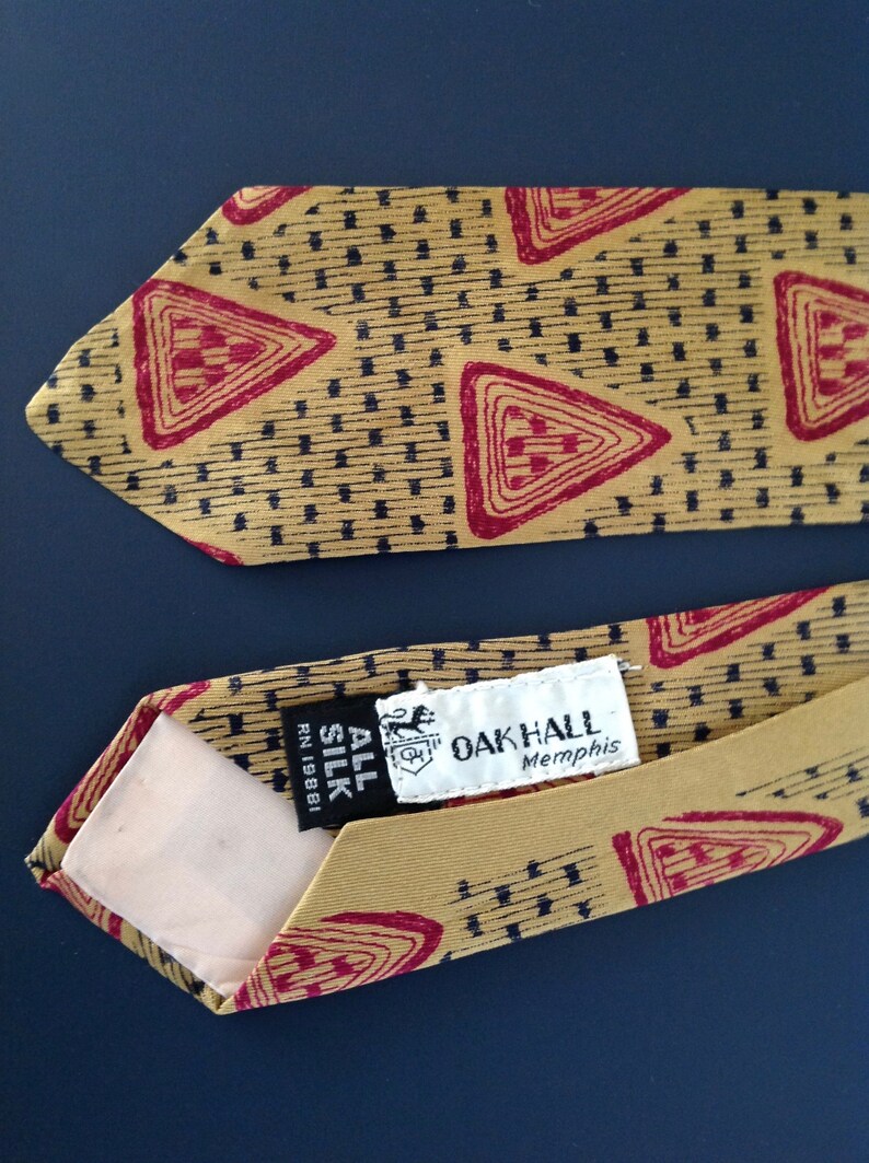 May include: A gold tie with a red and black geometric pattern. The tie has a label that reads "Oak Hall Memphis" and "All Silk RN 19881".