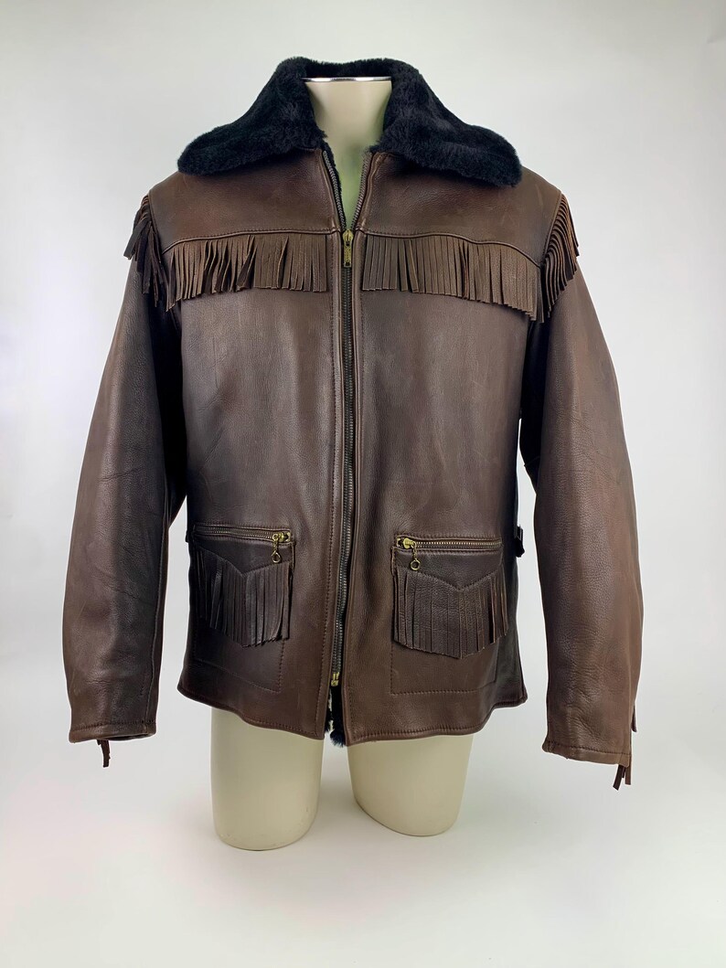 May include: Brown leather jacket with a black faux fur collar and fringe detailing. The jacket features a zip-up front, two front pockets with fringe, and a classic Western style. A stylish outerwear piece.
